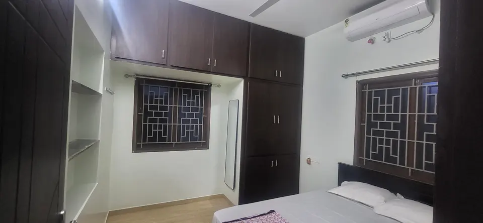 Master bedroom with a cot, wall-mounted split air-conditioner, wardrobe and loft cabinets, and grilled windows on two walls