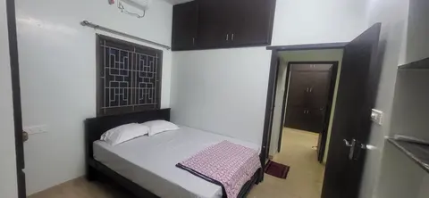 Cot below a grilled window, with the bedroom door open to the passage