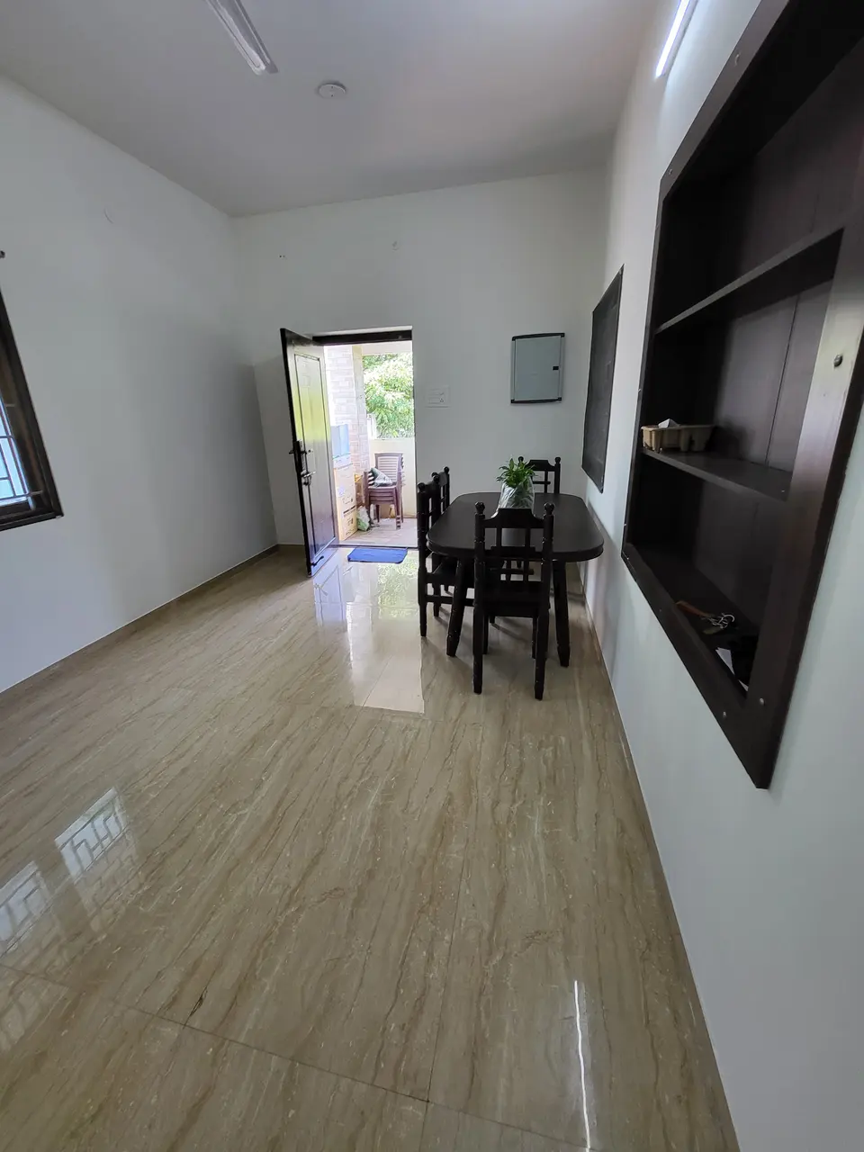 Living hall with a wooden dining table and chairs, and the open door to the porch