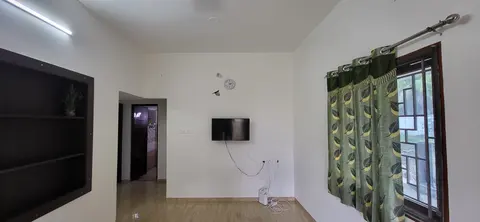 Living hall with a wall-mounted TV, built-in shelf unit and patterned curtains
